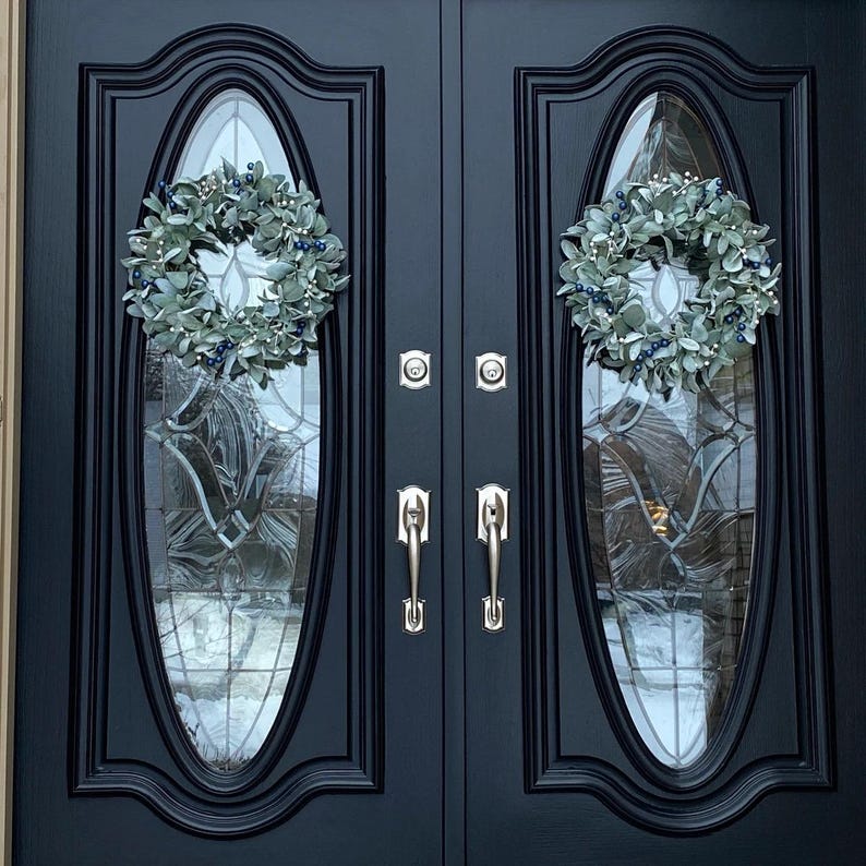 May include: A pair of black double doors with oval glass panels and silver door handles. Each door is decorated with a silver and green wreath.