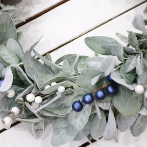 May include: A wreath made of faux lambs ear greenery with white and blue berries.