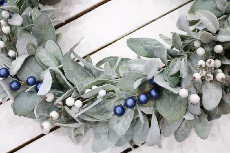 May include: A wreath made of faux lambs ear greenery with white and blue berries.