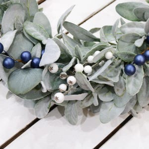 May include: A wreath made of faux lambs ear greenery with white and blue berries.