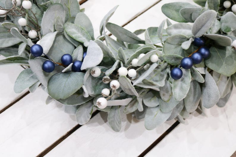 May include: A wreath made of faux lambs ear greenery with white and blue berries.