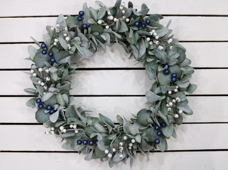 May include: A green wreath with white and blue berries. The wreath is made of artificial greenery and is perfect for decorating for the holidays.