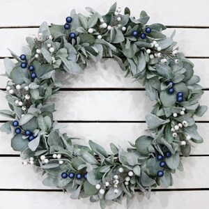 May include: A silver and blue wreath made of eucalyptus leaves with white berries and blue berries.