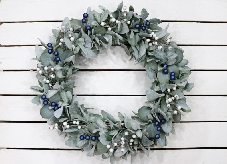 May include: A silver and blue wreath made of eucalyptus leaves with white berries and blue berries.