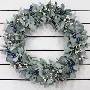 May include: A silver and blue Christmas wreath made of eucalyptus leaves with white berries and blue ornaments.