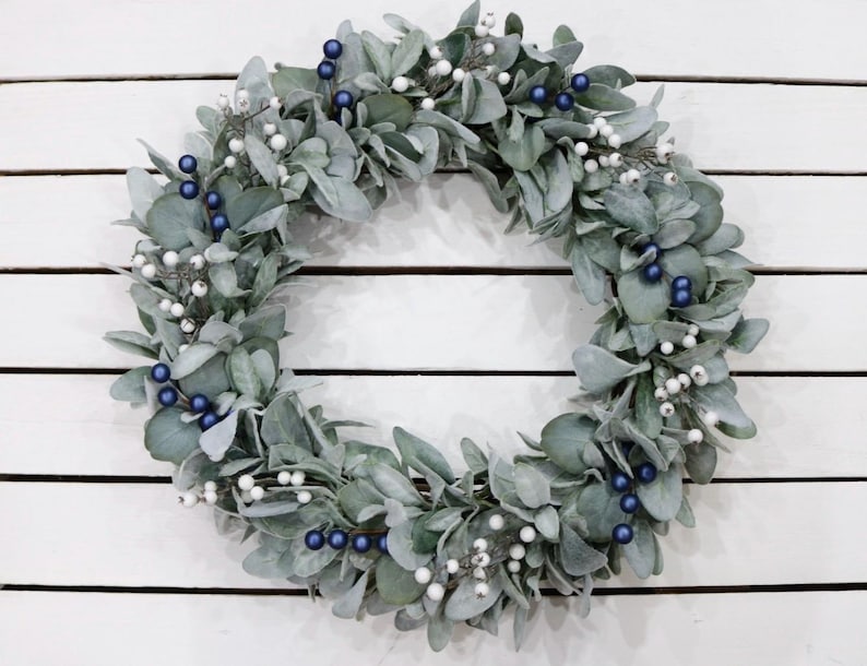 May include: A silver and blue Christmas wreath made of eucalyptus leaves with white berries and blue ornaments.