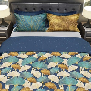 Peut inclure: Une housse de couette bleue et dorée avec un motif de feuilles de ginkgo. La housse de couette est sur un lit avec deux oreillers, l'un avec un motif or et bleu et l'autre avec un motif or.
