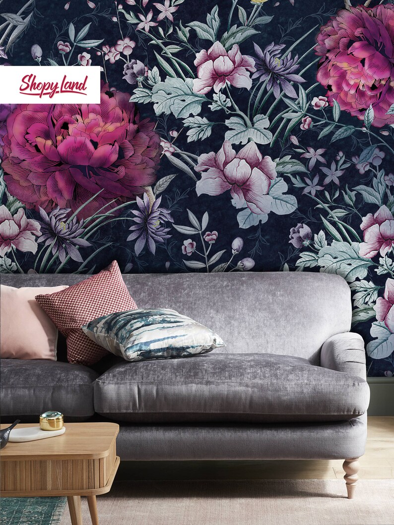 May include: A gray velvet sofa with three pillows, a wooden coffee table, and a rug. The sofa is in front of a wall with a floral wallpaper featuring pink and white flowers on a dark blue background. The text "Shopy Land" is visible in the top left corner of the image.