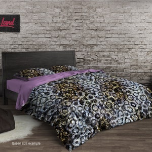 Puede incluir: Una cama de tamaño queen con una cabecera negra y una funda nórdica estampada. La funda nórdica presenta un patrón abstracto en negro, blanco y dorado. La cama está hecha con una almohada estampada en morado y blanco y una almohada blanca.