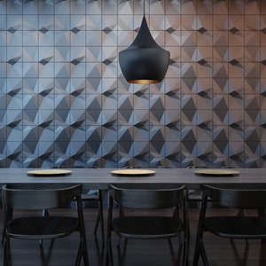 Op de afbeelding: Een rechthoekige eettafel van donker hout met drie zwarte houten stoelen en drie lichtgekleurde borden. Een zwarte hanglamp hangt boven de tafel, tegen een muur bedekt met donkergrijze, driedimensionale geometrische vierkante tegels.
