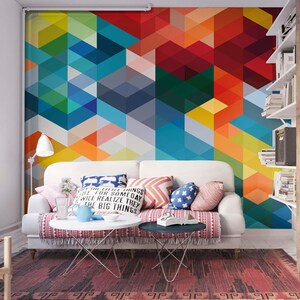 Può includere: Soggiorno con divano bianco, cuscini colorati e murale geometrico. Tavolino rotondo con teiera blu e oggetti decorativi. Tappeto fantasia e porta in legno completano l'arredamento della stanza.