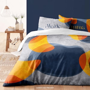May include: Queen size bedding set with a gray background and large abstract shapes in navy blue, orange, and yellow. The pillowcases have the names "Mark" and "Emma" printed on them. The words "Queen Size Preview" are printed at the bottom.