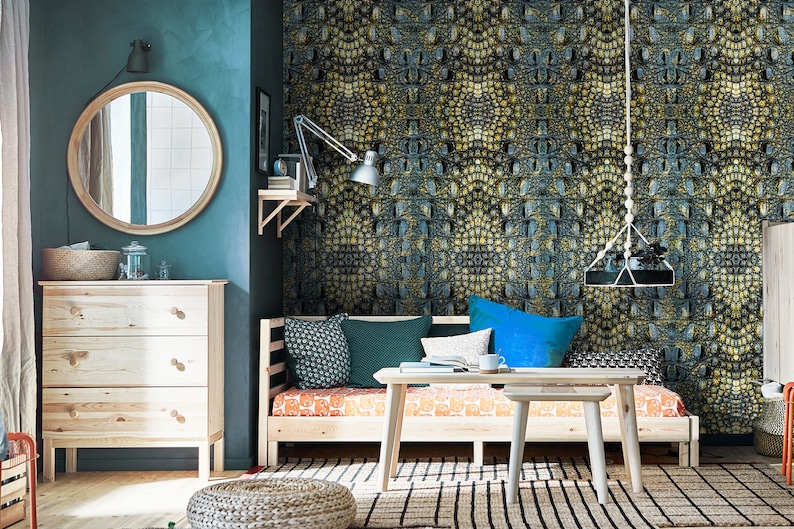 May include: A teal blue room with a wooden daybed with green and blue pillows. The daybed is in front of a wall with a crocodile skin patterned wallpaper. There is a wooden coffee table in front of the daybed and a wooden dresser to the left of the daybed.