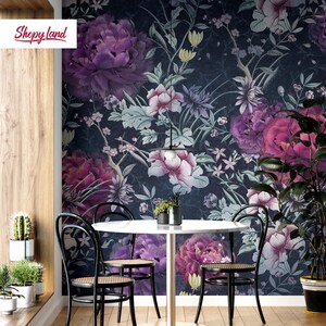 May include: A dining room with a round white table and four black chairs. The wall is covered in a dark floral wallpaper with purple, pink, and white flowers. A black pendant light hangs above the table.