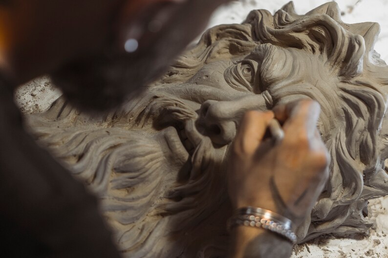 May include: A person sculpting a detailed clay bust of a bearded man with a serious expression. The bust is unfinished, with the artist's hand visible as they work on the face.