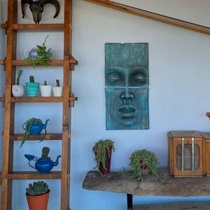 May include: A wooden ladder shelf displays potted cacti and succulents, including a blue teapot planter. A teal-colored face sculpture hangs on the wall. A ram skull decorates the top of the shelf, adding a rustic touch to the interior.