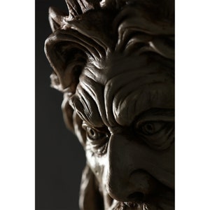 May include: Close-up of a detailed, sculpted face with a furrowed brow and intense eyes. The face is made of a light brown material and appears to be part of a larger sculpture.