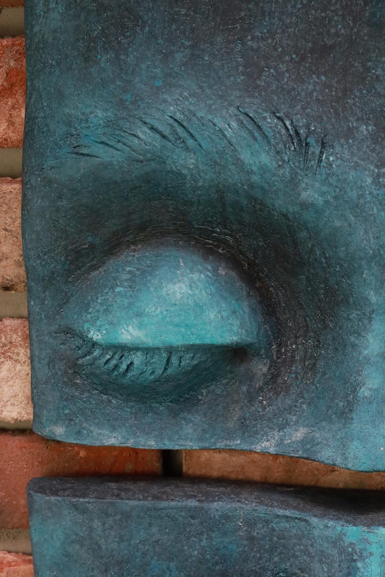 May include: Close-up of a teal-colored sculpture of a closed eye. The eye is set against a backdrop of a brick wall. The sculpture has a textured surface and is painted in shades of teal and black.