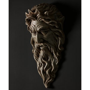 May include: A detailed, white plaster sculpture of a man's face with a long beard and a crown of thorns. The sculpture is mounted on a dark gray wall.