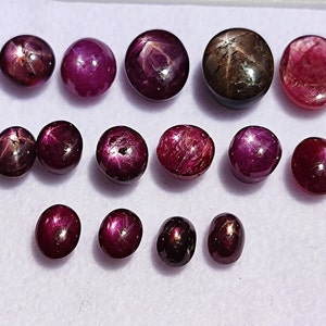 Op de afbeelding: Assortiment van twaalf rode en zwarte ster-robijn edelstenen. De edelstenen zijn van verschillende groottes en vormen, sommige hebben een meer ovale vorm en andere zijn rond.