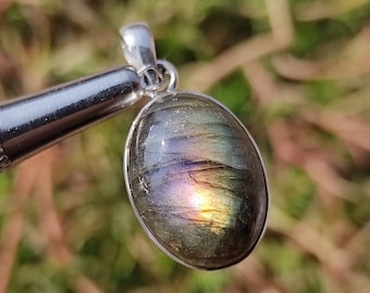 Può includere: Un ciondolo d'argento con una grande pietra ovale di labradorite. La pietra preziosa ha una base grigio scuro con riflessi iridescenti blu, verdi e dorati.