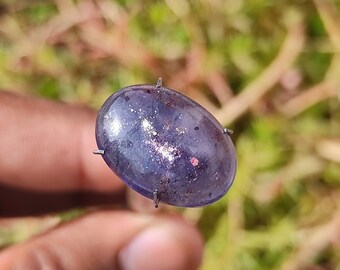 May include: A close-up of a blue gemstone with silver flecks and a metallic sheen. The gemstone is oval-shaped and is set in a silver bezel.