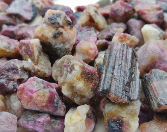 May include: A collection of rough, natural gemstones in various shades of pink, brown, and black. The stones are tumbled and have a smooth, polished finish.