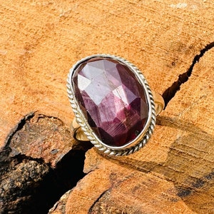 May include: A silver ring featuring a large, oval-shaped, faceted purple gemstone set in a twisted silver band.