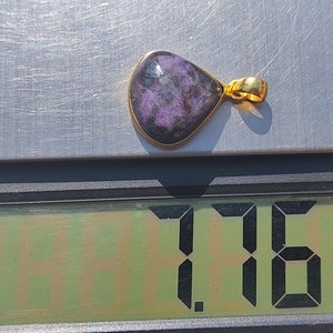 Pode incluir: Um pingente roxo e dourado com uma pedra em forma de l&aacute;grima. O pingente pesa 1,76 gramas.