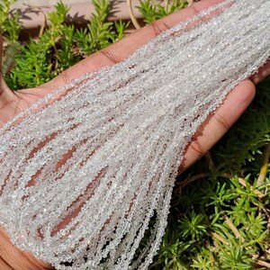 Puede incluir: Una hebra de cuentas de cristal transparente y facetadas. Las cuentas son pequeñas y tienen una forma de diamante. La hebra es larga y se sostiene en una mano.