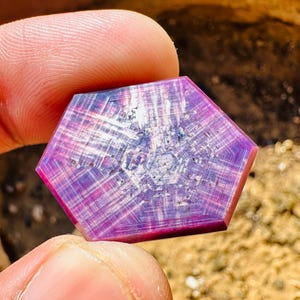 Puede incluir: Una piedra preciosa facetada, púrpura y rosa, con un patrón en forma de estrella. La piedra preciosa está cortada en forma hexagonal.