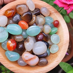 May include: A bowl of assorted agate stones in various colors, including white, brown, red, green, and blue. The stones are smooth and polished, and they are arranged in a random pattern.