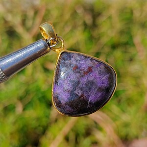 Pode incluir: Um pingente em forma de l&aacute;grima com uma gema roxa e marrom engastada em uma moldura de metal dourado.