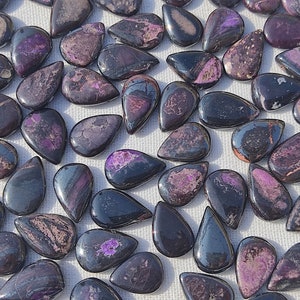 May include: A collection of purple and black teardrop-shaped gemstone cabochons. The stones have a natural, polished finish and are ready for jewelry making.