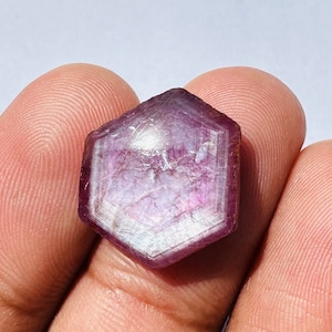 Może przedstawiać: Facetkowany fioletowy kamień szlachetny o sześciokątnym kształcie. Kamień szlachetny ma jasnofioletowy odcień z nutą różu.