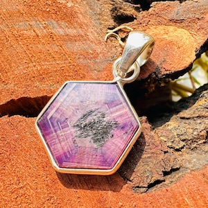 Peut inclure: Un pendentif hexagonal avec une pierre précieuse violette et noire sertie dans de l'argent sterling. La pierre précieuse présente un motif en étoile.
