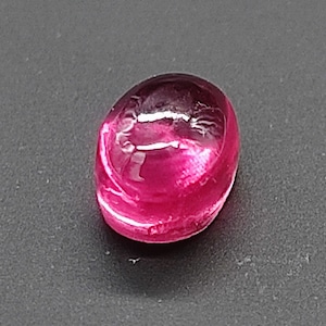 Może przedstawiać: Owalny, żywy różowy kamień szlachetny o gładkiej, wypolerowanej powierzchni.