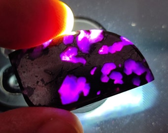 Puede incluir: Primer plano de una piedra preciosa púrpura y negra con un patrón único. La piedra preciosa está iluminada con una luz brillante, destacando su color vibrante.