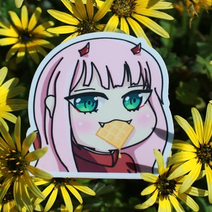 May include: A pink and red anime character sticker with green eyes and pink hair, eating a waffle with syrup dripping down. The sticker is placed on a background of yellow flowers.