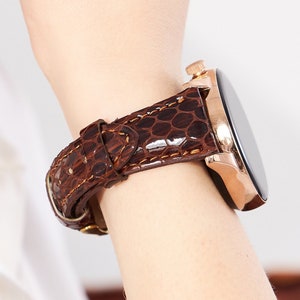 May include: A brown leather watch strap with a crocodile pattern. The watch face is black and round with a gold bezel.