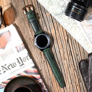 May include: A green leather watch band with white stitching. The band is attached to a black smartwatch with a round face.