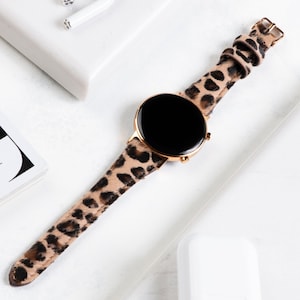 Puede incluir: Un reloj inteligente dorado con una esfera negra y una correa de estampado de leopardo.