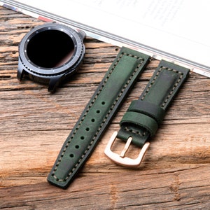 May include: Two green leather watch bands with white stitching and a rose gold buckle. The bands are laid out on a wooden surface.