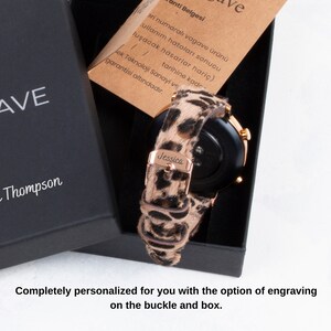 Puede incluir: Un reloj inteligente negro con una banda de oro rosa y una correa de estampado de leopardo. El reloj est&aacute; en una caja negra con el nombre "Jessica" grabado en la correa. La caja tambi&eacute;n tiene el texto "AVE Thompson" en la parte delantera.