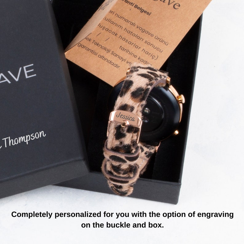 Puede incluir: Un reloj inteligente negro con una banda de oro rosa y una correa de estampado de leopardo. El reloj est&aacute; en una caja negra con el nombre "Jessica" grabado en la correa. La caja tambi&eacute;n tiene el texto "AVE Thompson" en la parte delantera.