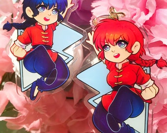 May include: Two anime character keychains with blue and red hair. The characters are wearing red and gold outfits and are posed in a fighting stance. The keychains are made of clear acrylic and have a blue background.