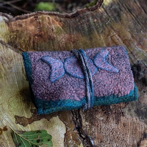 Op de afbeelding: Een klein, paars en turquoise gevoerd zakje met een geborduurd drievoudig maansikkel symbool op de voorkant. Het zakje wordt dichtgeknoopt met een bruin leren bandje.