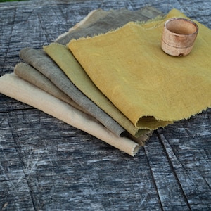 Può includere: Un mucchio di cinque campioni di tessuto in tonalità di verde e giallo, con un bordo grezzo e non rifinito. I campioni sono disposti in un gradiente di colore, con la tonalità più chiara in alto e la tonalità più scura in basso. Il tessuto è piegato ordinatamente e sembra essere fatto di lino o cotone.