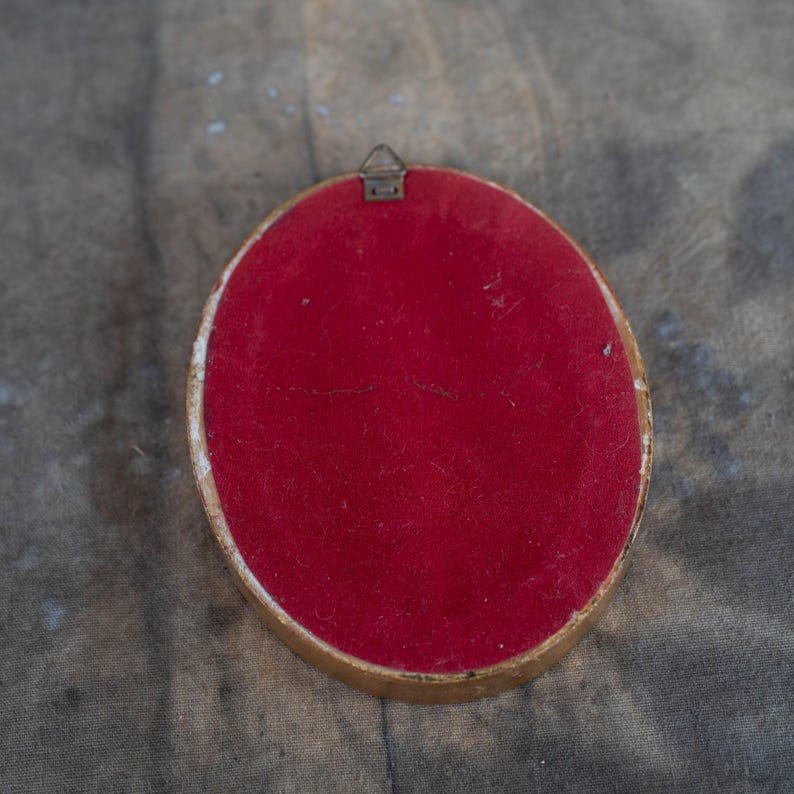 The reverse side of the oval miniature frame, covered in red backing material with a small hanging loop at the top.