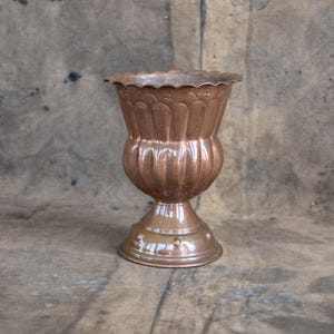 Peut inclure: Un vase de style vintage, de couleur cuivrée, avec un corps cannelé et un bord festonné. Le vase a une base de piédestal avec des détails décoratifs. Le design général est orné et élégant, adapté aux compositions florales ou à l'exposition décorative.